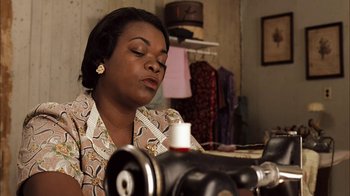 Movie still from “Honeydripper” (2007), directed by John Sayles – A woman sitting in front of a sewing machine in a room; Close Up shot, High angle