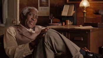 Movie still from “Honeydripper” (2007), directed by John Sayles – An older man sitting on a chair in a room; Medium shot, Over the shoulder angle