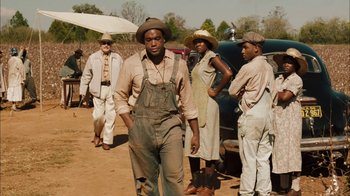 Movie still from “Honeydripper” (2007), directed by John Sayles – A group of men standing next to each other on a dirt field; Medium shot, Over the shoulder angle