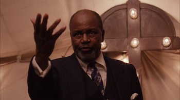 Movie still from “Honeydripper” (2007), directed by John Sayles – A man in a suit and tie waving at the camera; Close Up shot, Low angle