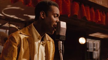 Movie still from “Honeydripper” (2007), directed by John Sayles – A man in a yellow jacket is singing into a microphone; Medium shot, Over the shoulder angle