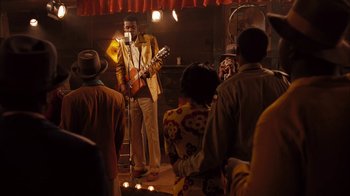 Movie still from “Honeydripper” (2007), directed by John Sayles – A man in a yellow jacket holding a guitar on a stage; Wide shot, Over the shoulder angle