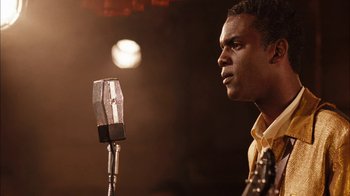 Movie still from “Honeydripper” (2007), directed by John Sayles – A man standing in front of a microphone in a room; Close Up shot, Over the shoulder angle
