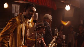 Movie still from “Honeydripper” (2007), directed by John Sayles – A group of people that are standing around a microphone; Medium shot, Over the shoulder angle