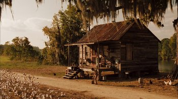 Movie still from “Honeydripper” (2007), directed by John Sayles – An old wooden shack with a person standing on the side of the road; Extreme Wide shot, High angle