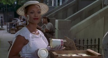 Movie still from “Hoodlum” (1997), directed by Bill Duke – A woman in a hat holding a box of cookies; Medium shot, Low angle
