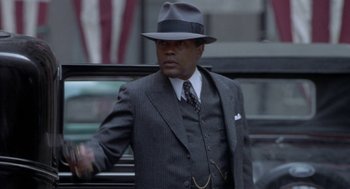 Movie still from “Hoodlum” (1997), directed by Bill Duke – A man in a suit and hat standing next to a car; Medium shot, Over the shoulder angle