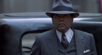 Movie still from “Hoodlum” (1997), directed by Bill Duke – A man wearing a suit and hat in front of a car; Close Up shot, Over the shoulder angle