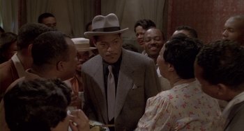 Movie still from “Hoodlum” (1997), directed by Bill Duke – A man wearing a suit and tie talking to a group of people; Medium shot, High angle