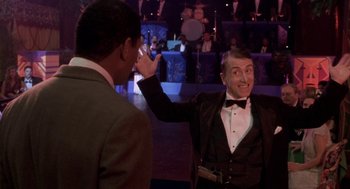 Movie still from “Hoodlum” (1997), directed by Bill Duke – A man in a suit and a bow tie is waving at another man in a suit and a bow tie in front of an audience; Medium shot, Over the shoulder angle