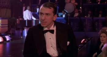 Movie still from “Hoodlum” (1997), directed by Bill Duke – A man in a tuxedo sitting in front of a group of people; Close Up shot, Over the shoulder angle