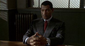 Movie still from “Hoodlum” (1997), directed by Bill Duke – A man sitting at a table wearing a suit; Medium shot, High angle