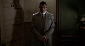 Movie still from “Hoodlum” (1997), directed by Bill Duke – A man in a suit and tie standing in a room; Medium shot, Over the shoulder angle
