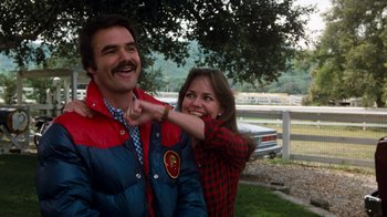 Movie still from “Hooper” (1978), directed by Hal Needham – A man and a woman standing next to each other under a tree; Medium shot, Over the shoulder angle