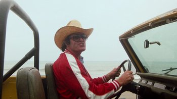 Movie still from “Hooper” (1978), directed by Hal Needham – A man wearing a cowboy hat driving a car on the beach; Medium shot, Low angle