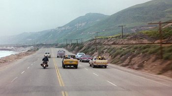 Movie still from “Hooper” (1978), directed by Hal Needham – A group of cars driving down a road next to a hill; Extreme Wide shot, High angle