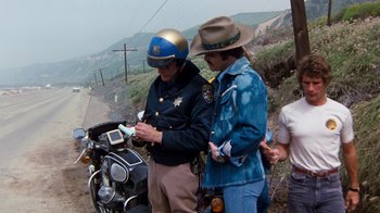 Movie still from “Hooper” (1978), directed by Hal Needham – A police officer is looking at a cell phone; Medium shot, High angle