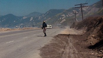 Movie still from “Hooper” (1978), directed by Hal Needham – A man riding a skateboard down the side of a road; Extreme Wide shot, High angle