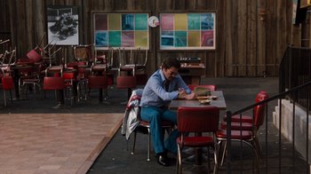 Movie still from “Hooper” (1978), directed by Hal Needham – A man sitting at a table in front of a clock; Wide shot, High angle