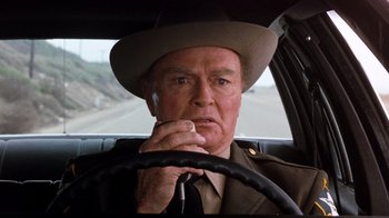 Movie still from “Hooper” (1978), directed by Hal Needham – An older man wearing a hat sitting in the drivers seat of a car; Close Up shot, Over the shoulder angle