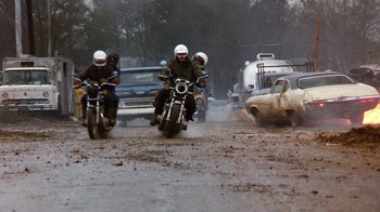 Movie still from “Hooper” (1978), directed by Hal Needham – A group of men riding motorcycles down a muddy road; Wide shot, Low angle