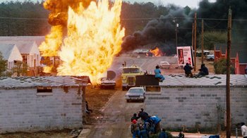 Movie still from “Hooper” (1978), directed by Hal Needham – A street scene with a truck on fire and people sitting on the side of the road; Extreme Wide shot, High angle