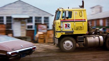 Movie still from “Hooper” (1978), directed by Hal Needham – A truck driving down a dirt road next to a car; Wide shot, Low angle
