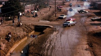 Movie still from “Hooper” (1978), directed by Hal Needham – Cars driving down a muddy road in the middle of the day; Extreme Wide shot, High angle
