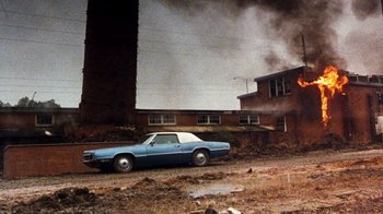 Movie still from “Hooper” (1978), directed by Hal Needham – An old car is parked in front of a brick building; Extreme Wide shot, High angle