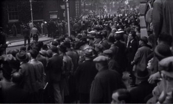 Movie still from “Hope and Glory” (1987), directed by John Boorman – A crowd of people standing on a street; Extreme Wide shot, High angle