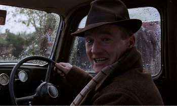 Movie still from “Hope and Glory” (1987), directed by John Boorman – A man wearing a hat sitting in the driver's seat of a car; Close Up shot, Low angle