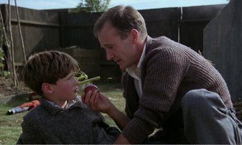 Movie still from “Hope and Glory” (1987), directed by John Boorman – A man and a boy are eating an apple together; Medium shot, Over the shoulder angle