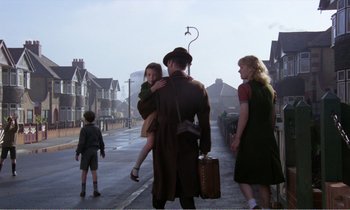 Movie still from “Hope and Glory” (1987), directed by John Boorman – A man holding a little girl in his arms while walking down the street; Wide shot, Low angle