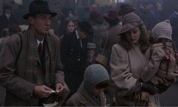 Movie still from “Hope and Glory” (1987), directed by John Boorman – A group of people standing around each other in a room; Medium shot, Over the shoulder angle