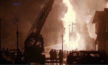 Movie still from “Hope and Glory” (1987), directed by John Boorman – A group of people standing next to a fire truck; Extreme Wide shot, Low angle