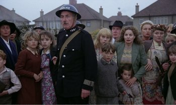Movie still from “Hope and Glory” (1987), directed by John Boorman – A group of people standing in front of a building; Medium shot, High angle