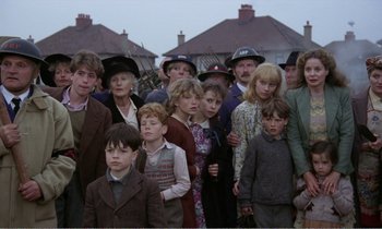 Movie still from “Hope and Glory” (1987), directed by John Boorman – A group of people standing in front of a row of houses; Medium shot, High angle