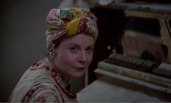 Movie still from “Hope and Glory” (1987), directed by John Boorman – A woman wearing a colorful head scarf sitting in front of a piano; Close Up shot, Over the shoulder angle