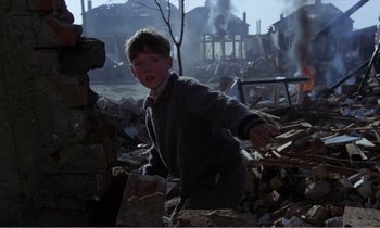 Movie still from “Hope and Glory” (1987), directed by John Boorman – A young boy standing in a pile of rubble; Medium shot, Low angle