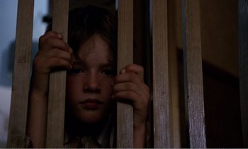 Movie still from “Hope and Glory” (1987), directed by John Boorman – A young child peering through the bars of a jail cell; Close Up shot, Low angle