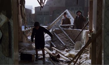 Movie still from “Hope and Glory” (1987), directed by John Boorman – A group of people standing around a building; Wide shot, High angle