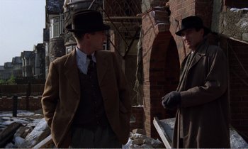 Movie still from “Hope and Glory” (1987), directed by John Boorman – Two men in suits and hats are standing outside; Medium shot, Over the shoulder angle