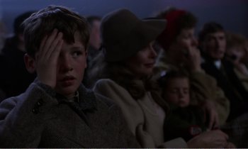 Movie still from “Hope and Glory” (1987), directed by John Boorman – A group of people sitting in a row watching a movie; Close Up shot, Over the shoulder angle