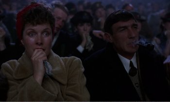 Movie still from “Hope and Glory” (1987), directed by John Boorman – A woman and a man sitting in front of an audience; Close Up shot, High angle