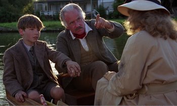 Movie still from “Hope and Glory” (1987), directed by John Boorman – A group of people sitting on top of a boat in the water; Medium shot, Over the shoulder angle