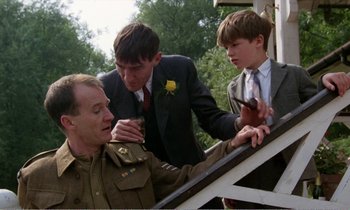 Movie still from “Hope and Glory” (1987), directed by John Boorman – Three young men in suits and ties looking at an older man in a uniform; Medium shot, Over the shoulder angle