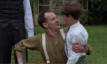Movie still from “Hope and Glory” (1987), directed by John Boorman – An older man and a young boy are hugging outside; Medium shot, Over the shoulder angle