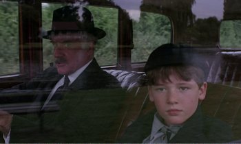 Movie still from “Hope and Glory” (1987), directed by John Boorman – A man and a young boy in a car; Medium shot, Over the shoulder angle