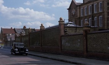 Movie still from “Hope and Glory” (1987), directed by John Boorman – An image of an old car parked on the side of the road; Extreme Wide shot, Low angle