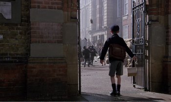 Movie still from “Hope and Glory” (1987), directed by John Boorman – A boy with a backpack walking down the street; Wide shot, High angle